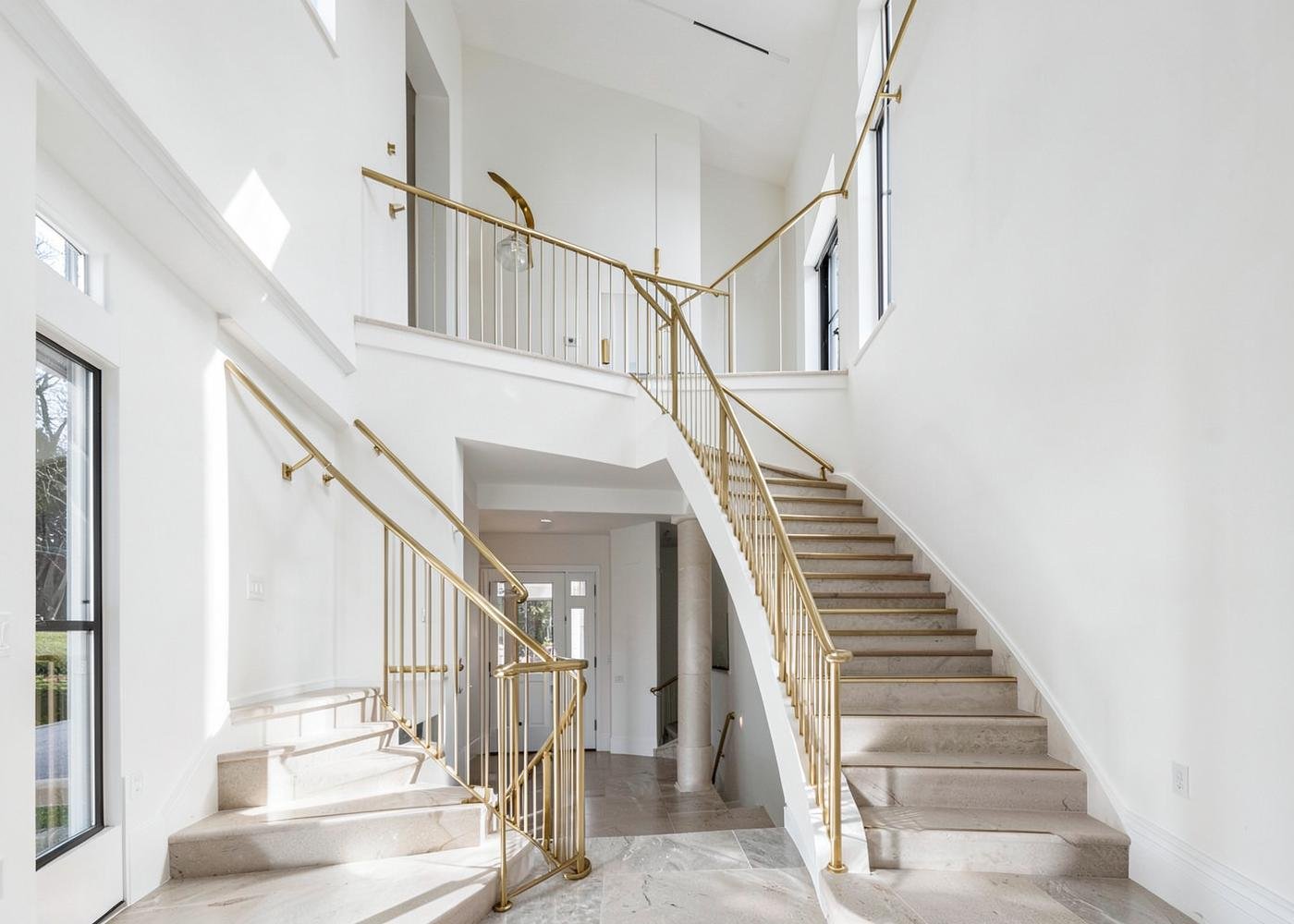 Double-height entrance hall with brass railing and marble stair in a completed home